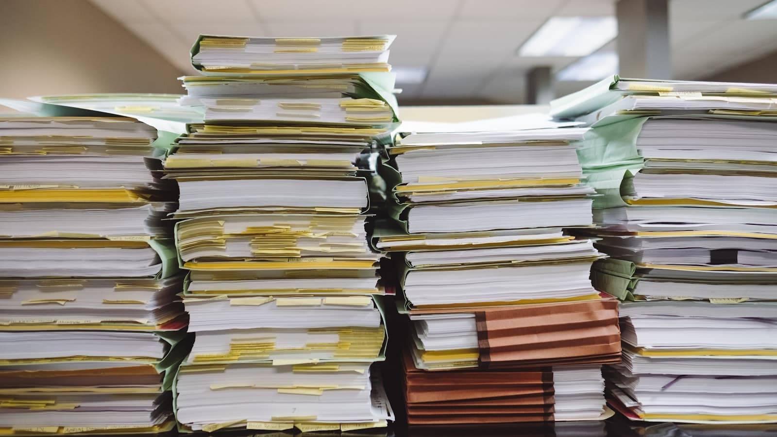 Tall stacks of paper files and folders with coloured index tabs in an office