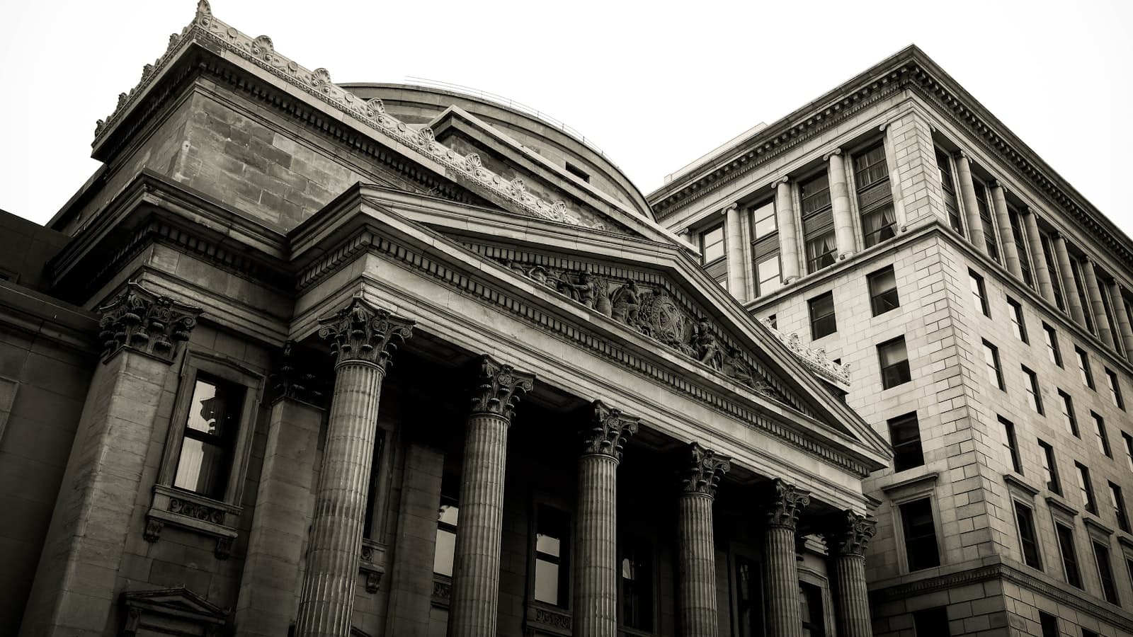 Low-angle black-and-white view of a classical stone bank building with columns and a dome