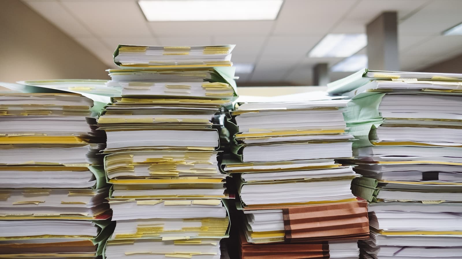 Tall stacks of paper files and folders with yellow index tabs in an office