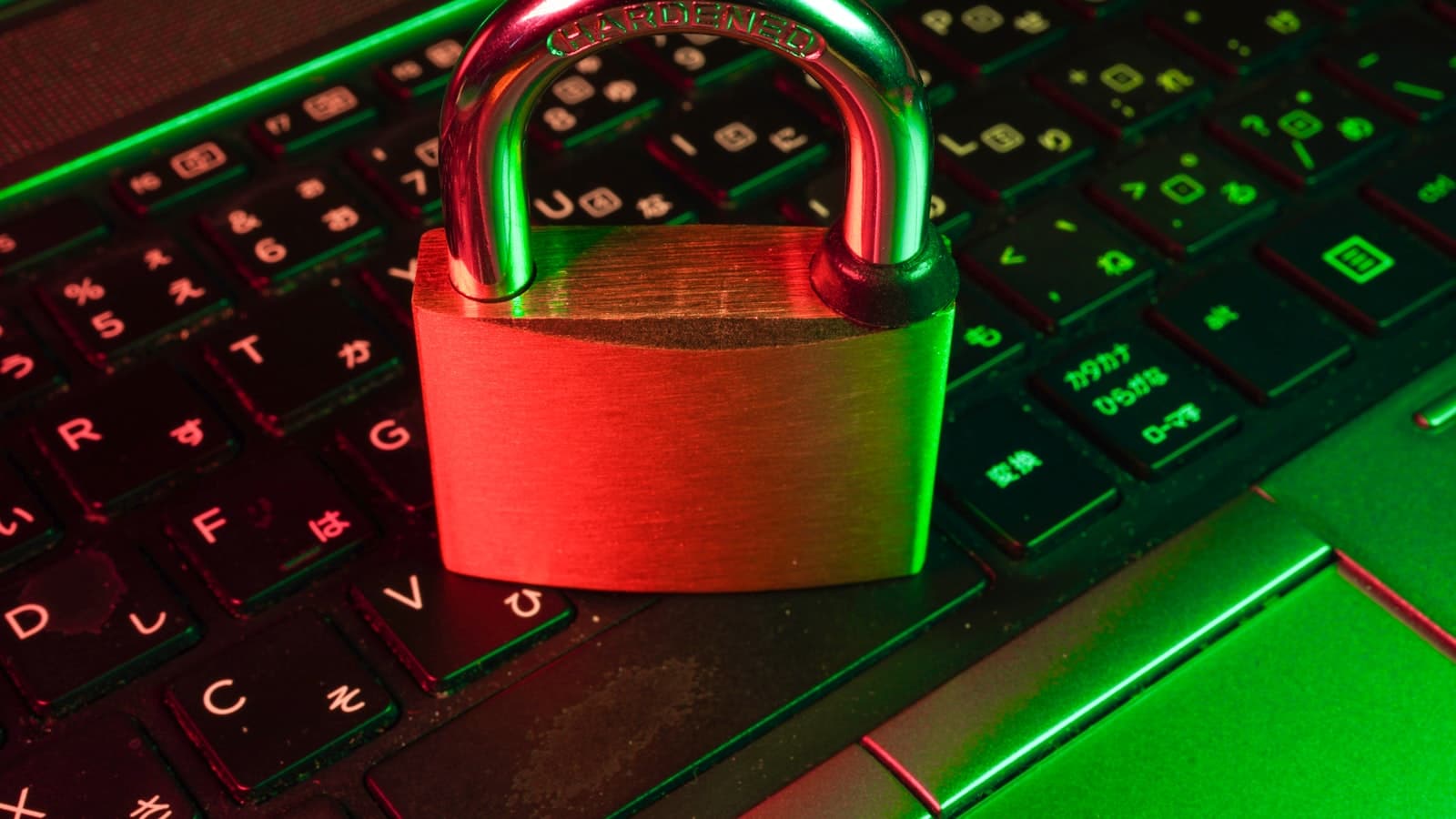 A brass padlock labelled HARDENED resting on a laptop keyboard under red and green light