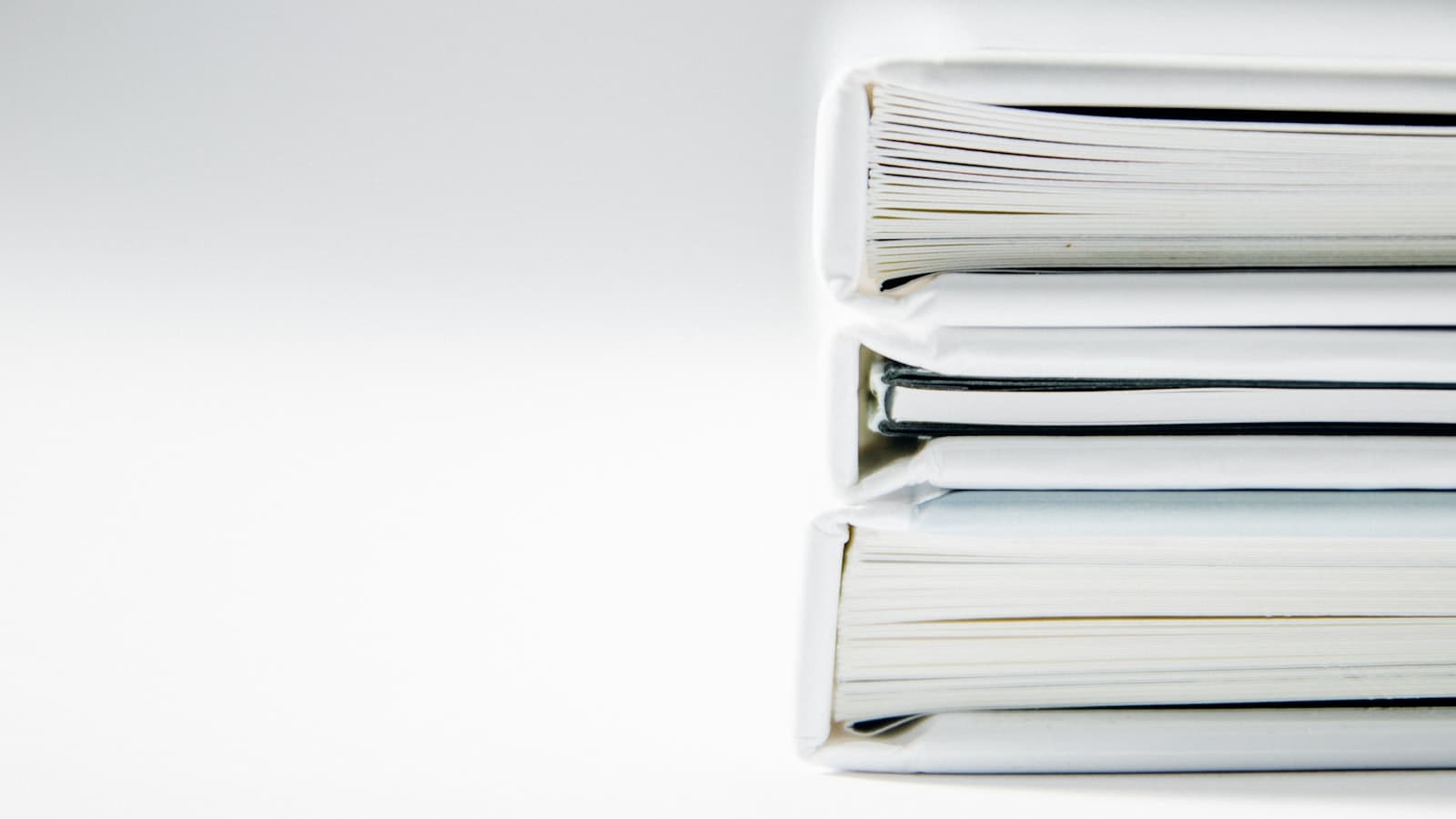 A stack of three thick white binders or document folders against a plain background