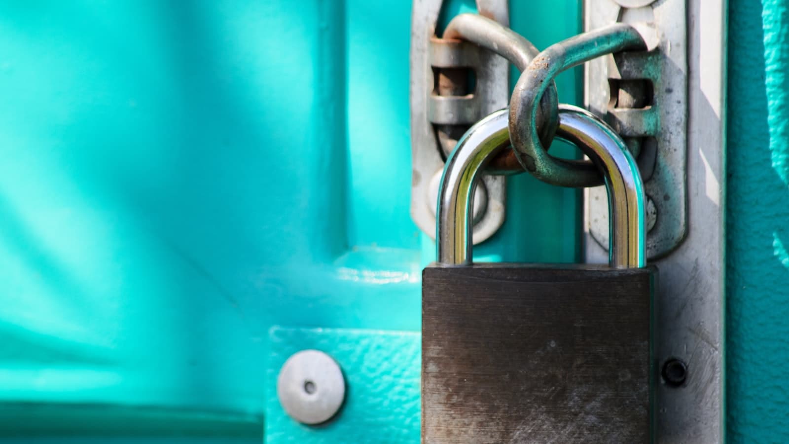 A metal padlock and chain securing a latch on a turquoise painted door
