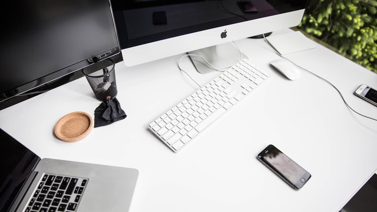 An iMac, keyboard, mouse, phone and laptop arranged on a white desk