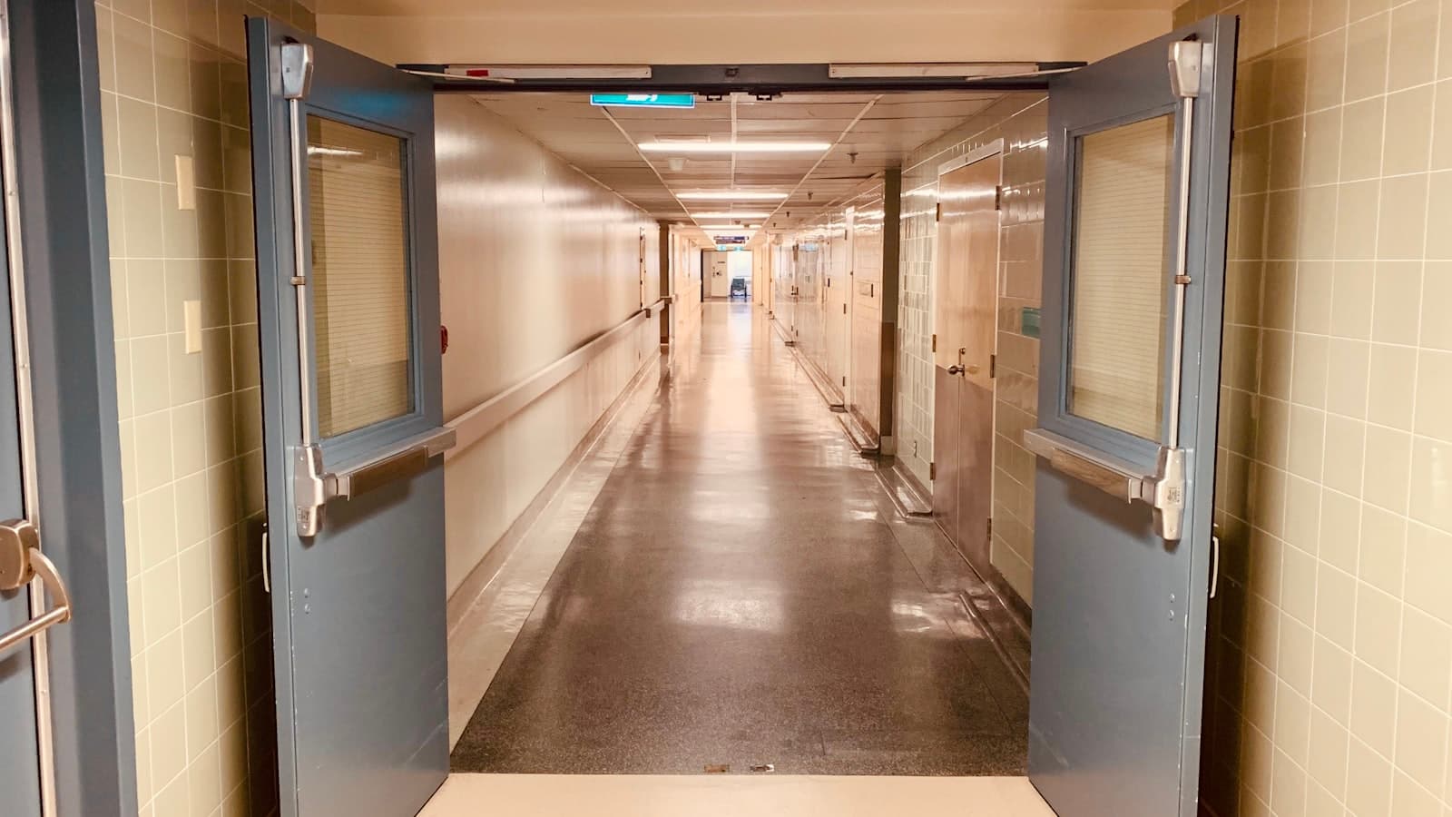 An empty hospital corridor seen through open double doors