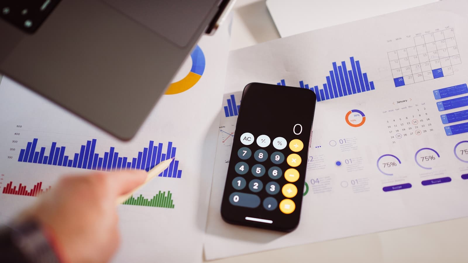 Overhead view of a hand with a pencil, a phone calculator and printed charts