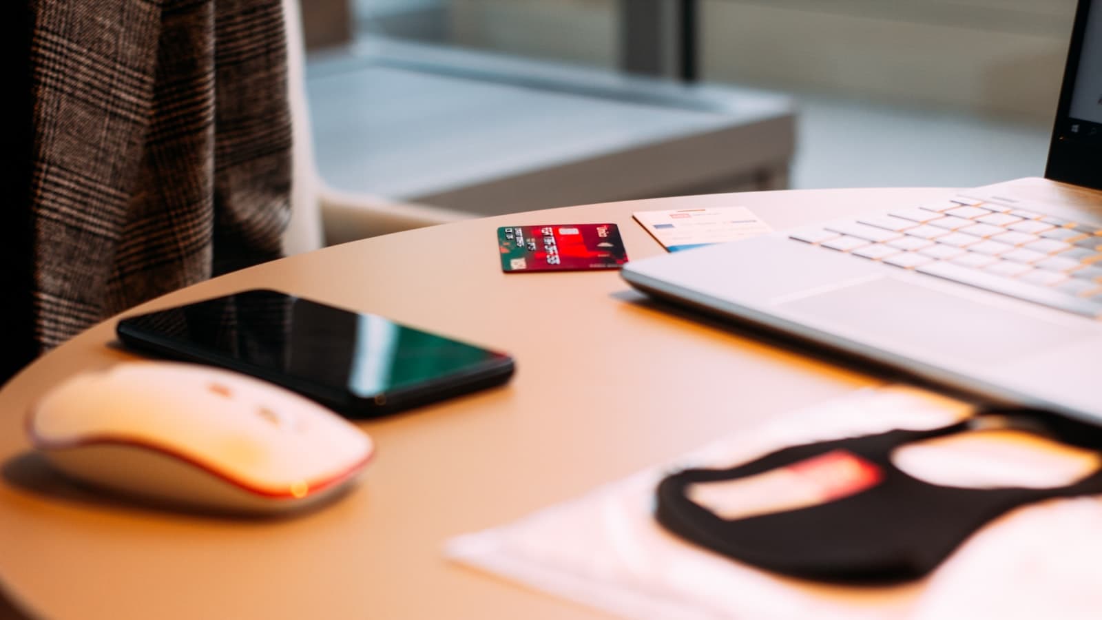 A laptop, smartphone, wireless mouse and a card on a round desk