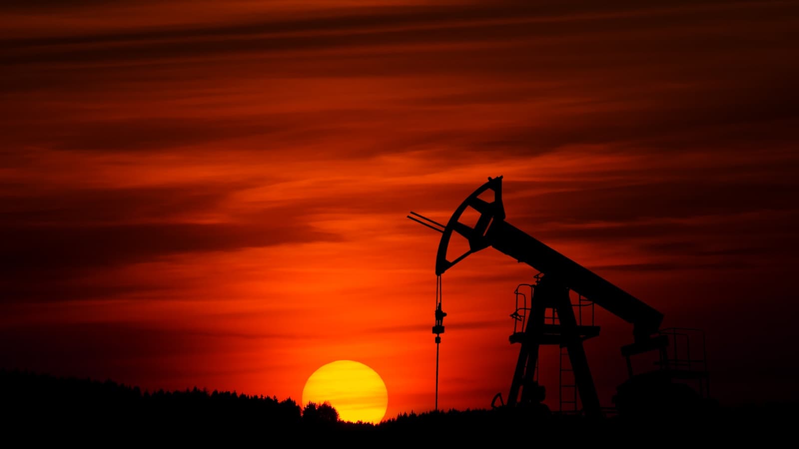 Silhouette of an oil pump jack against an orange sunset sky