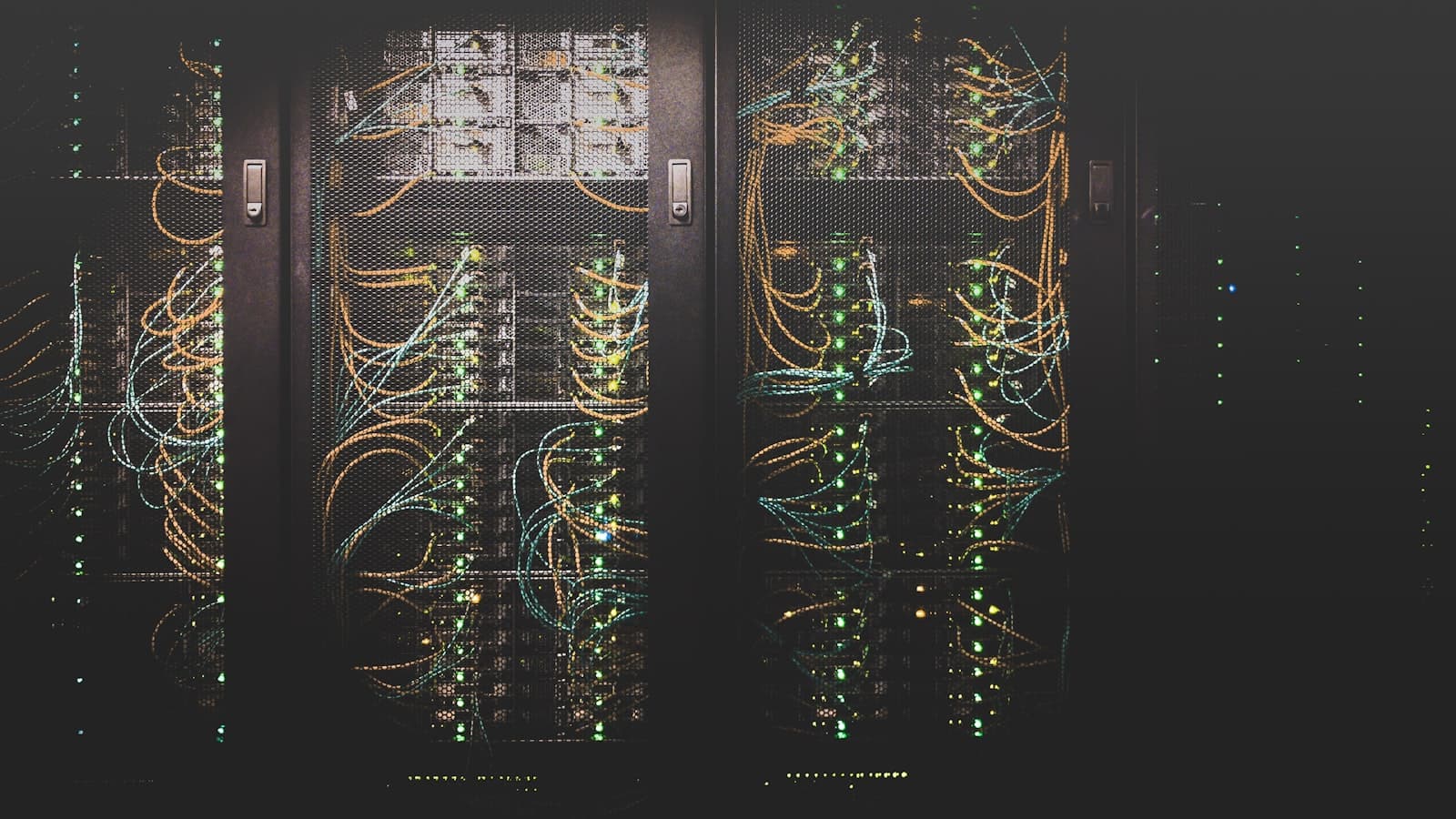 Rows of dark server racks with tangled coloured cabling behind mesh cabinet doors