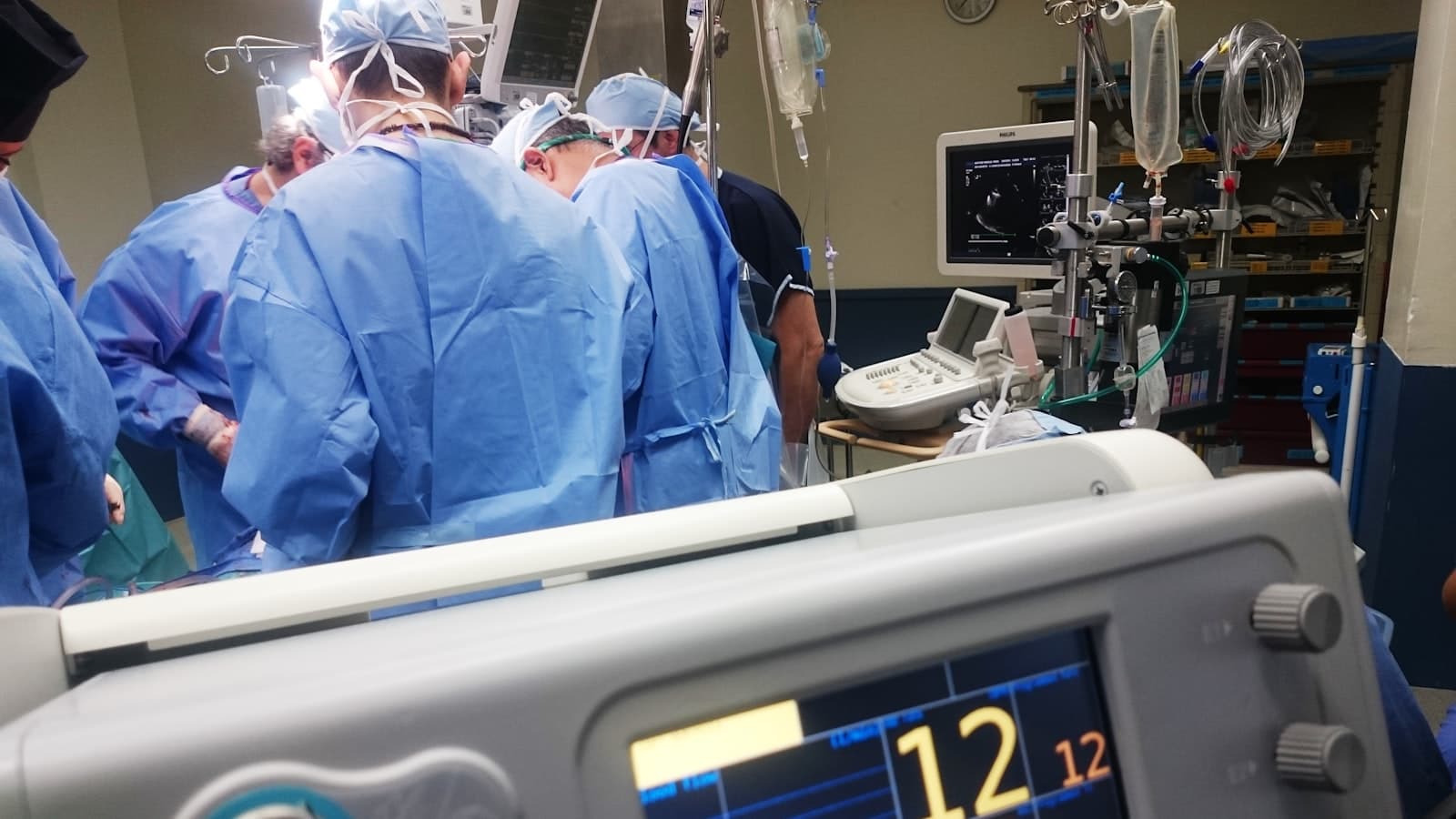 A surgical team in blue scrubs at work beside medical monitors in an operating room