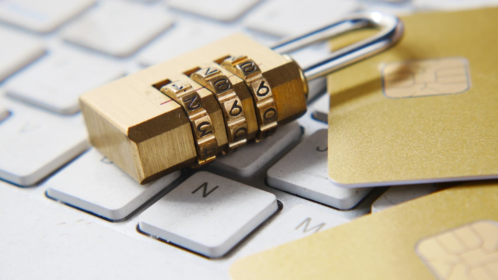 A brass combination padlock resting on a laptop keyboard beside gold chip cards