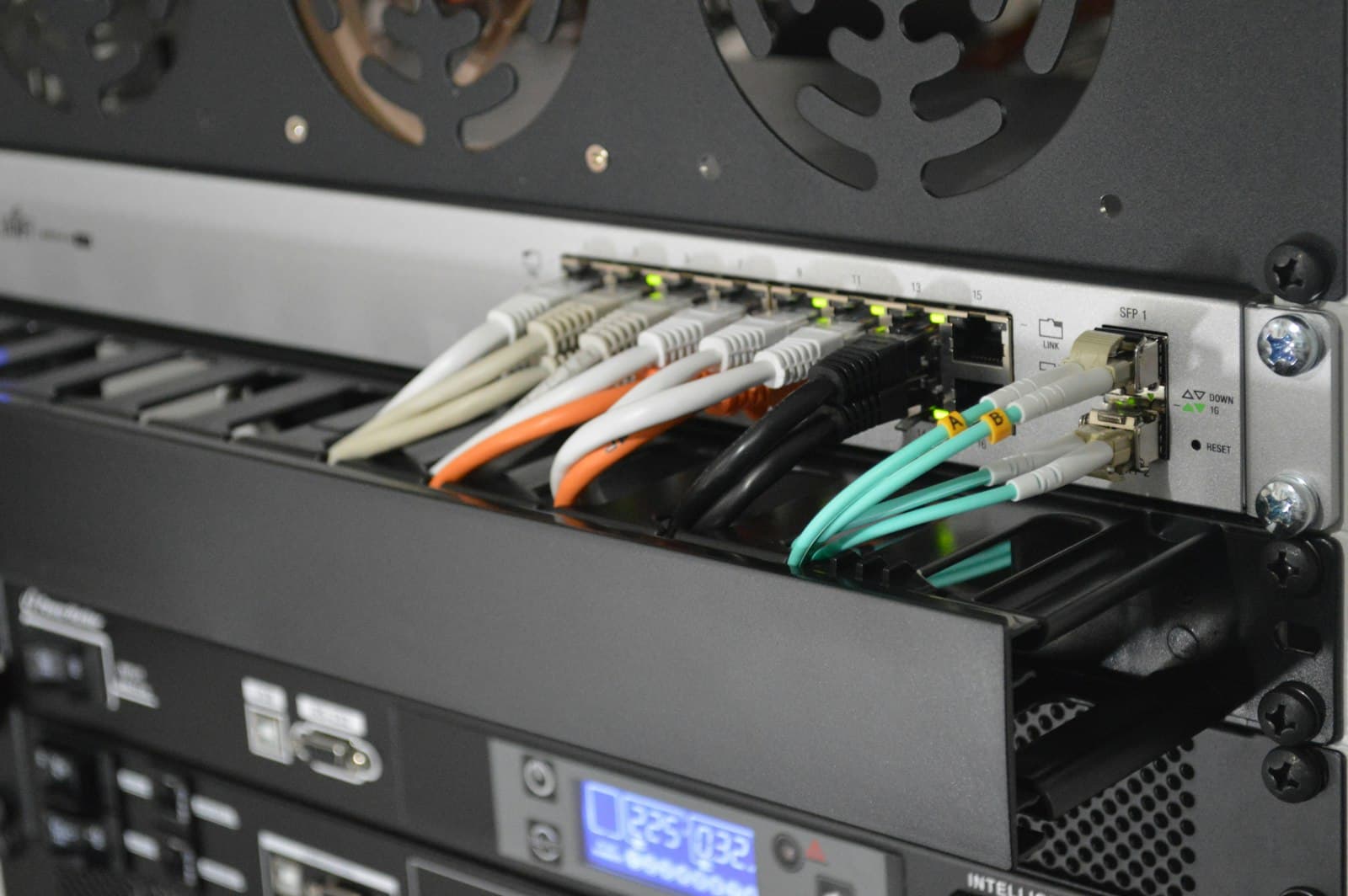 A rack-mounted network switch with patch and fibre uplinks connected, above a UPS