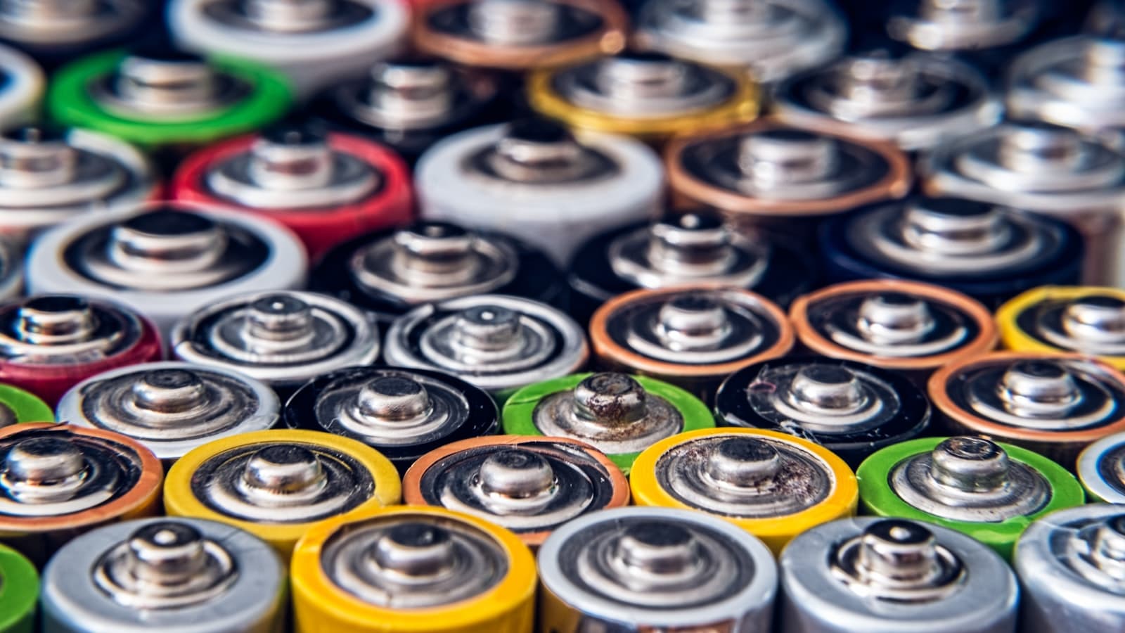 Close-up of the tops of many colourful used batteries packed together