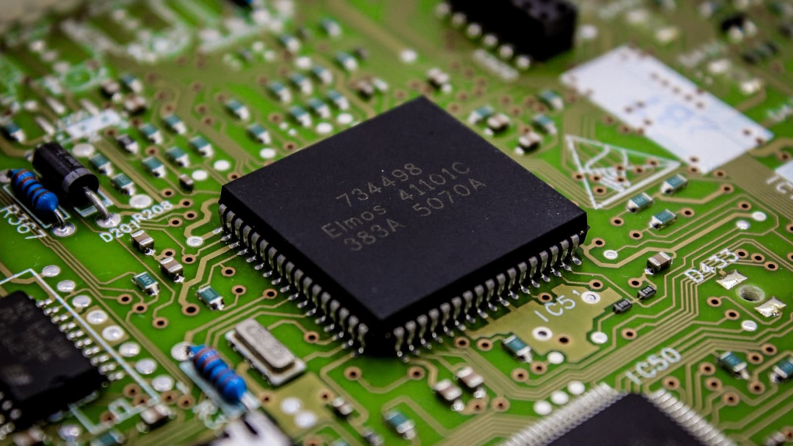 Close-up of a black microchip mounted on a green circuit board with components