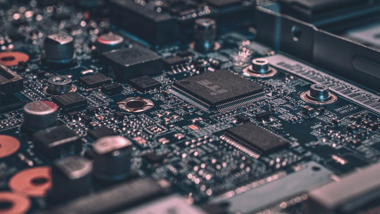 Close-up of a circuit board with a central microchip, capacitors and fine soldered traces