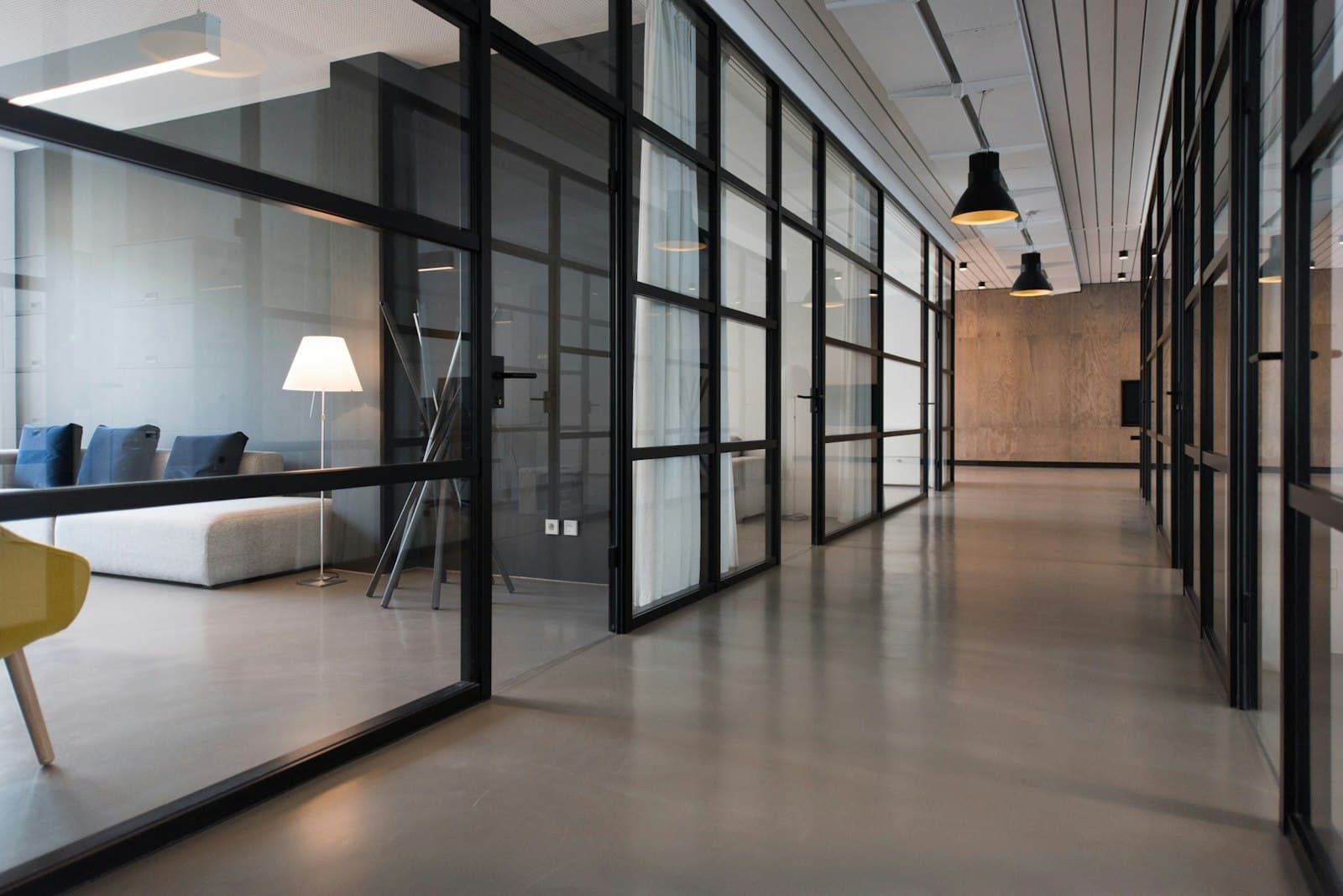 A modern enterprise office corridor lined with glass-partitioned meeting rooms
